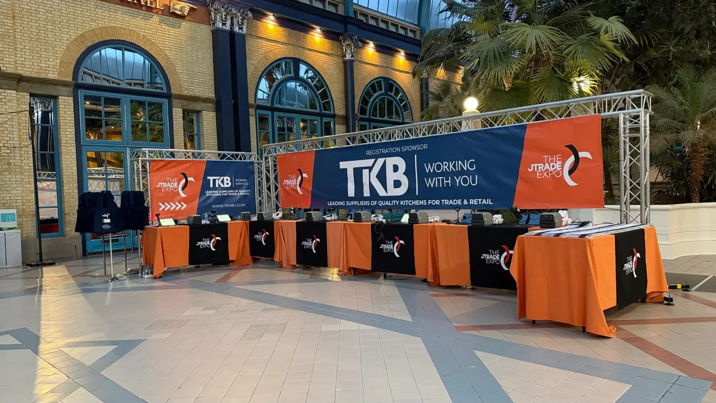 A truss gantry with sponsor banners over branded tables